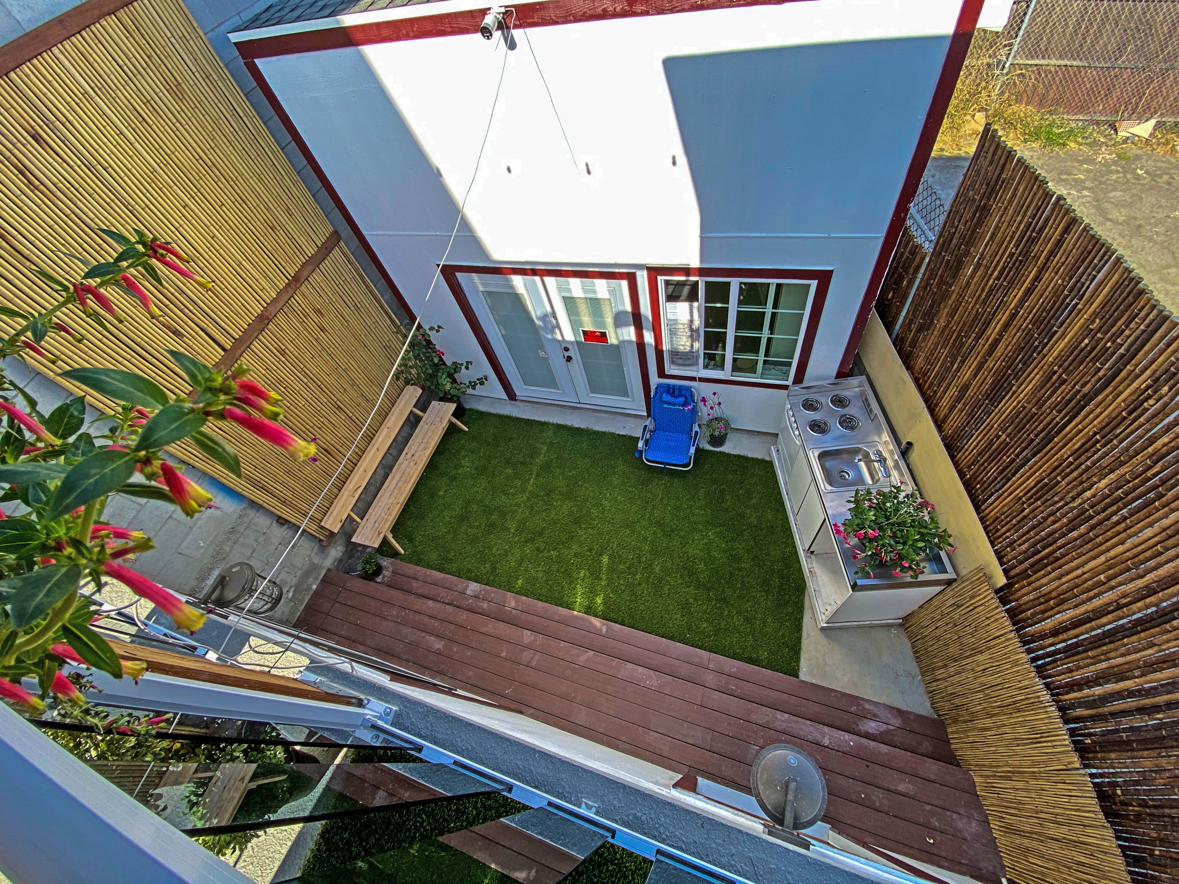 Une petite maison moderne avec une terrasse en bois, un petit jardin et une chaise bleue.