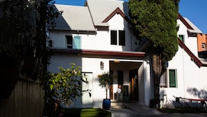 A two-story building with a white facade, a red roof, and a large tree in front.