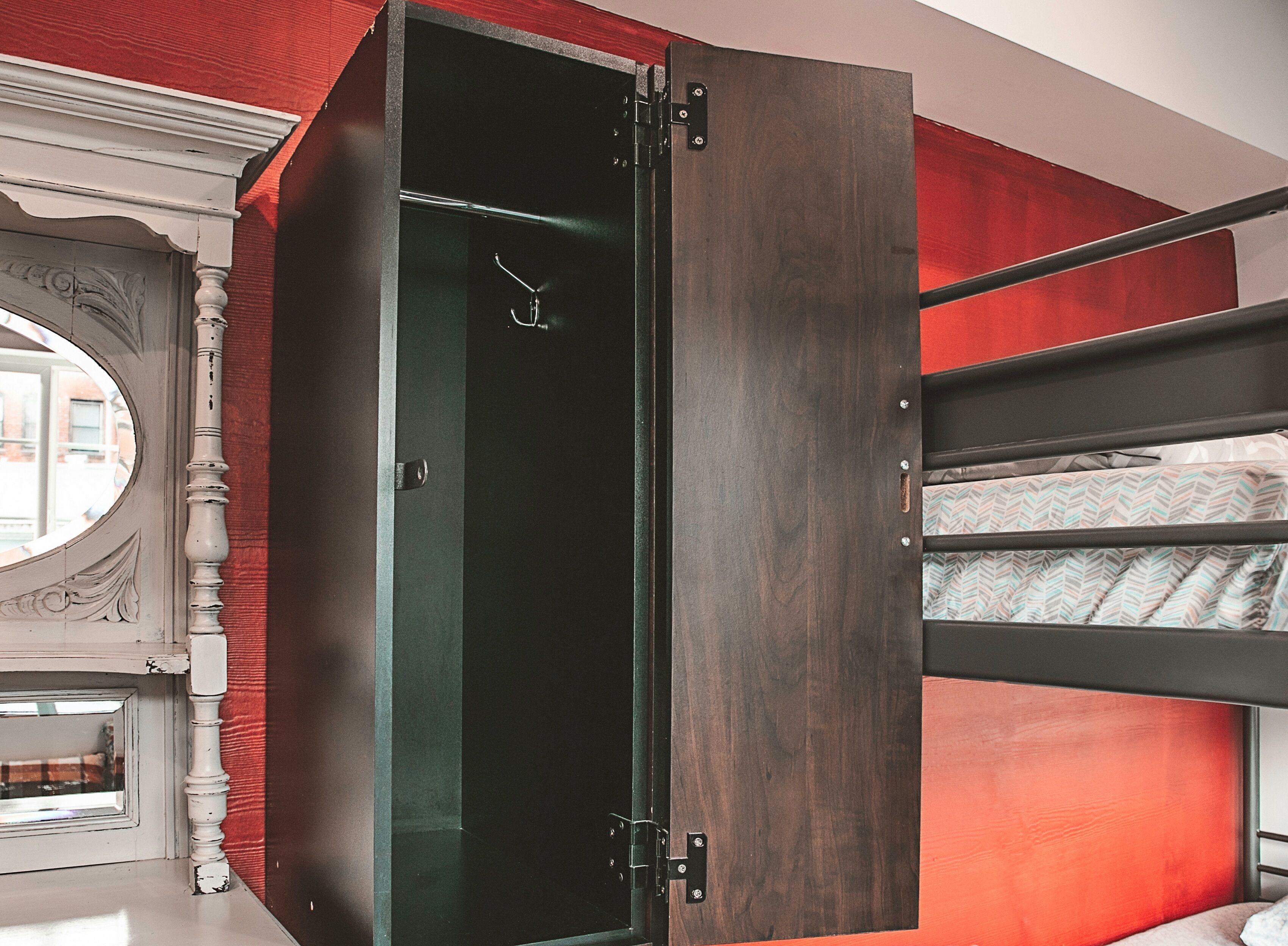 Une chambre avec un lit superposé, une armoire en bois foncé et un mur d’accent rouge.