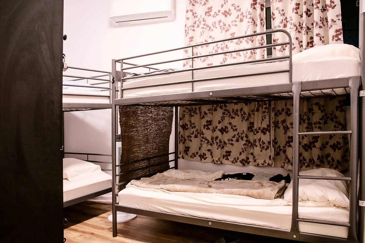 A bunk bed room with a wooden floor, a window with a curtain, and a door.
