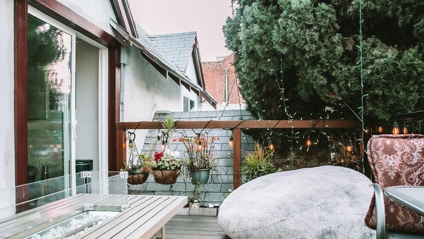 A wooden deck with a stone bench, a metal chair, and hanging plants.