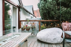 A wooden deck with a stone bench, a metal chair, and hanging plants. - The Rumi Hostel (Los Angeles)