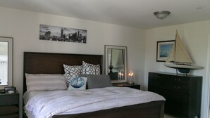 A bedroom with a large bed, a cityscape painting, a sailboat decoration, and a dresser. - Lynnwood Airport-Retreat (Lynnwood)