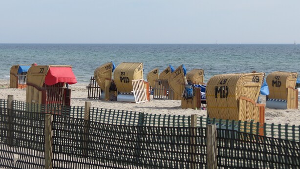 Cabañas de playa con números, una cerca y el mar al fondo.