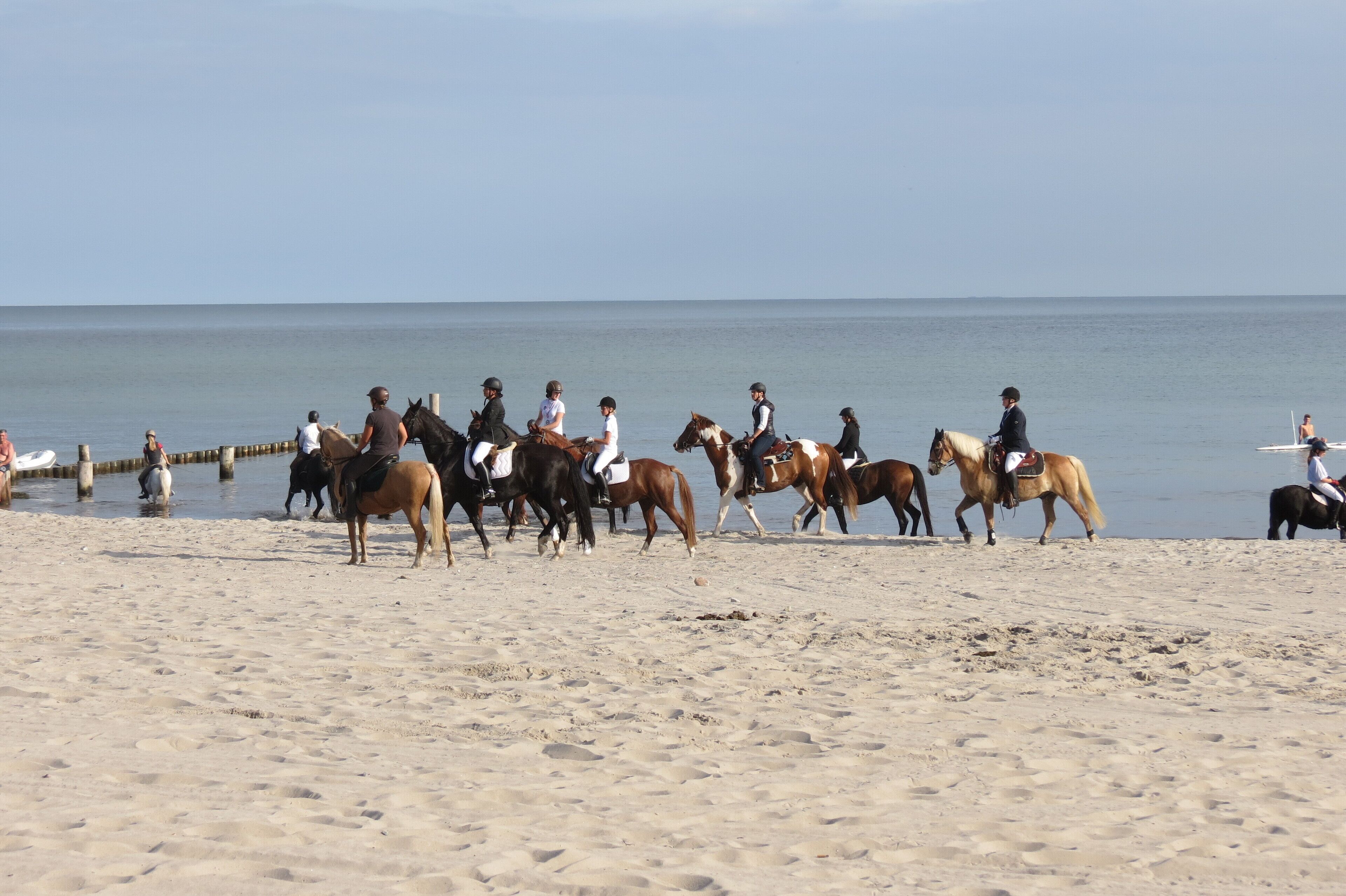 A beach with people riding horses along the shore.