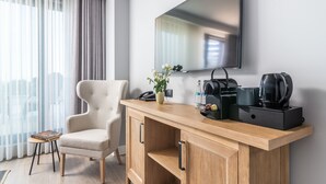 Una habitación de hotel moderna con una consola de madera, un sillón color crema, un televisor de pantalla plana y una cafetera.