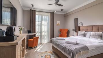 A hotel room with a bed, a desk, an orange chair, a television, and a ceiling fan.