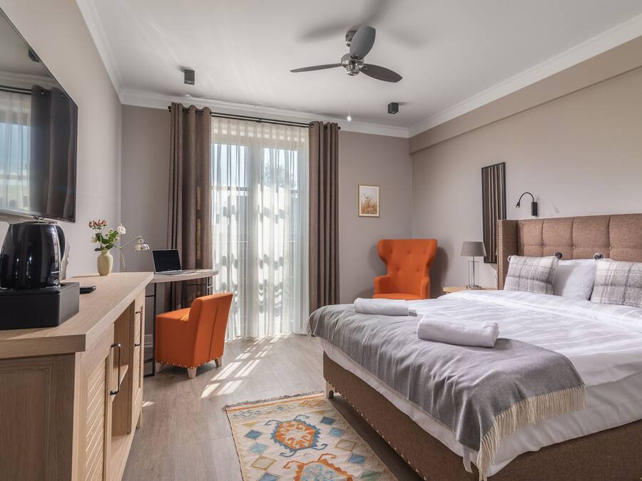 A hotel room with a bed, a desk, an orange chair, a television, and a ceiling fan.