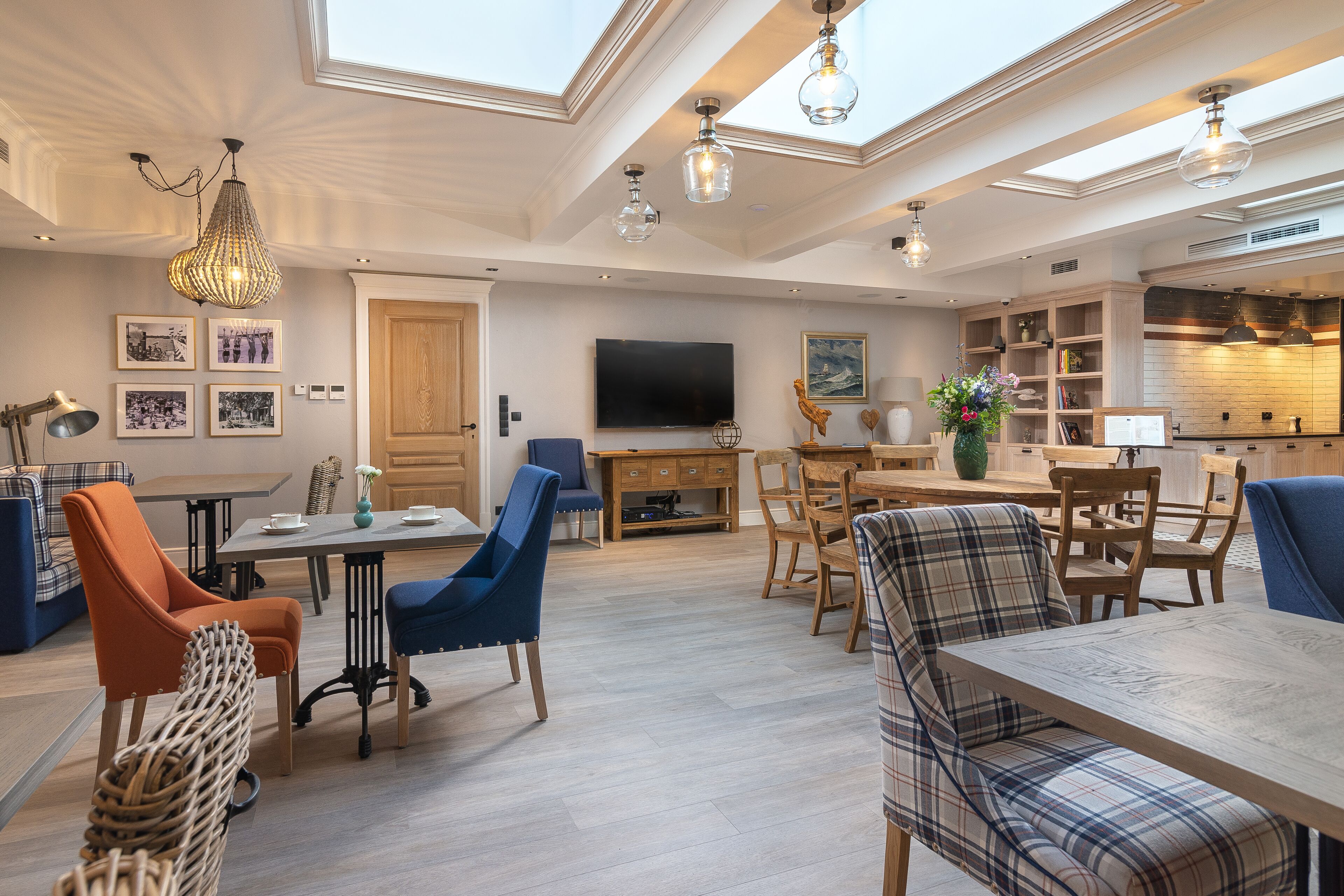 A spacious living area with a high ceiling, skylights, a dining table, and a television.