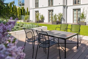 Un patio con mesa y sillas, rodeado de un jardín con diversas plantas y una valla.