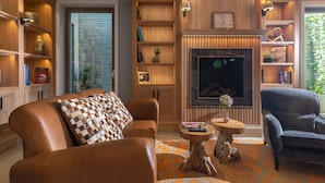 Una sala de estar acogedora con sofás de cuero, chimenea, estanterías de madera y un ventanal grande.