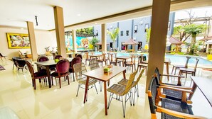 Un vaste espace de restauration intérieur, doté de nombreuses tables et chaises, et d’une grande fenêtre donnant sur une piscine et un jardin.