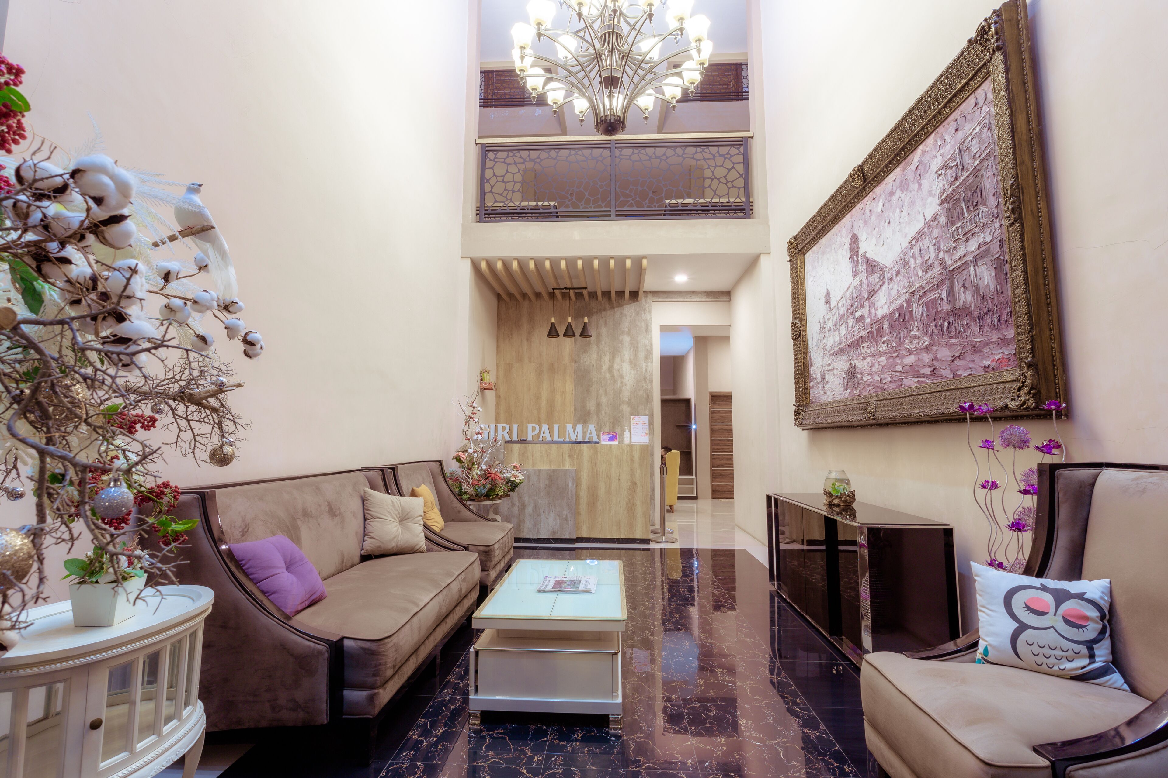 A hotel lobby with a reception desk, a chandelier, a large framed picture, and a seating area with a sofa and armchairs.