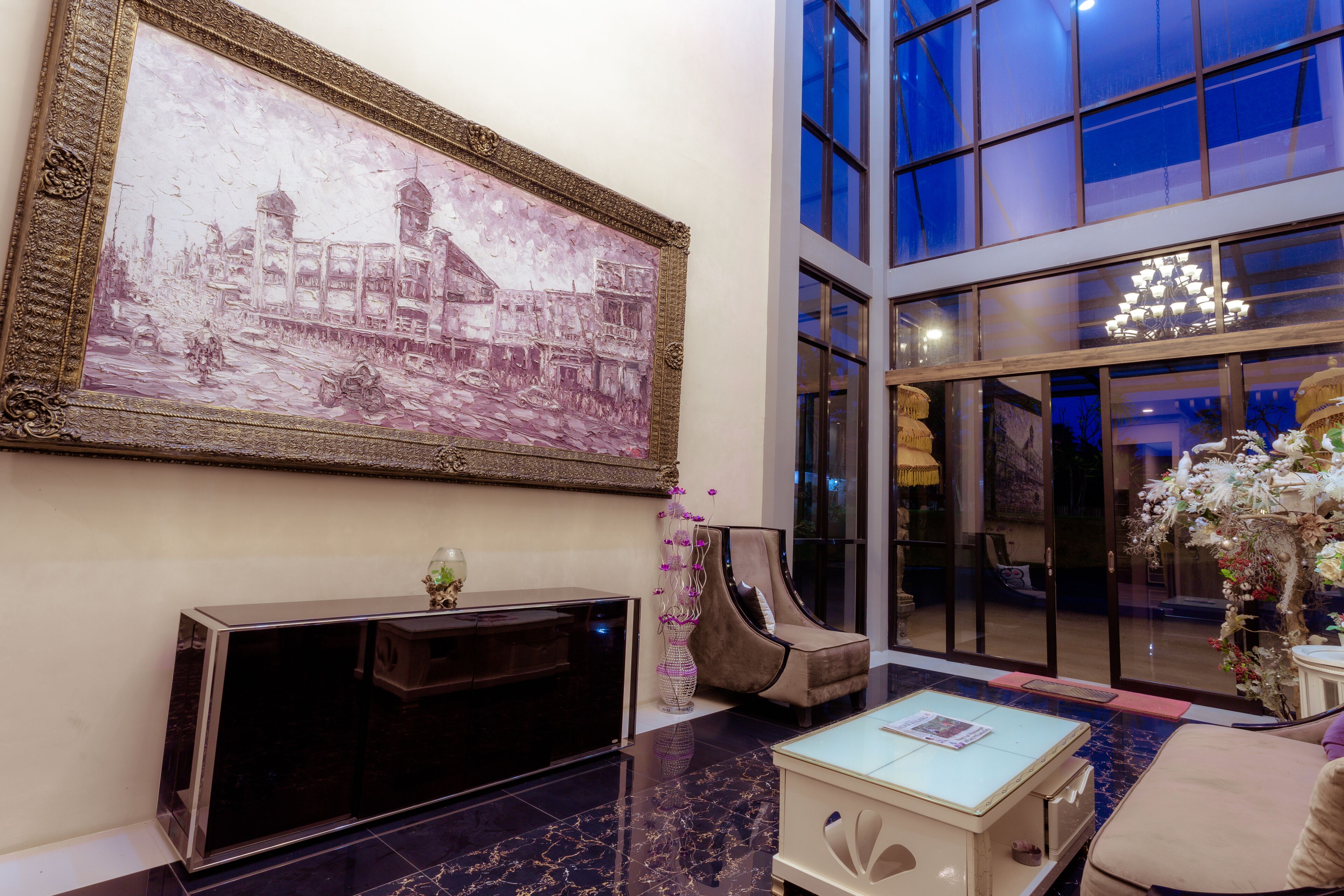A modern lobby with a large framed artwork, a sleek console table, a comfortable seating area, and a large window offering a view of the sky.