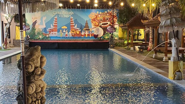 Une piscine avec une fresque murale en arrière-plan, une statue en pierre et des guirlandes lumineuses.
