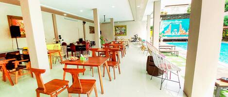 A spacious indoor dining area with wooden tables and chairs, a television, and a view of a swimming pool.