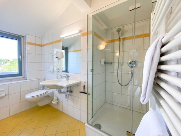 A bathroom with a glass-enclosed shower, a toilet, a sink, and a window.