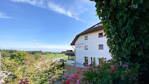 Un bâtiment blanc, sur lequel on peut lire l’inscription « Berggasthof Gochsten », est entouré d’une végétation luxuriante et de plantes en fleurs.