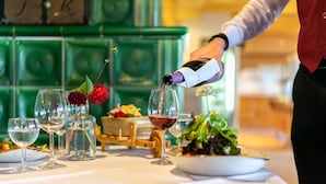Une table dressée avec des verres à vin, une bouteille de vin rouge dont on verse le contenu, et un saladier rempli de salade.