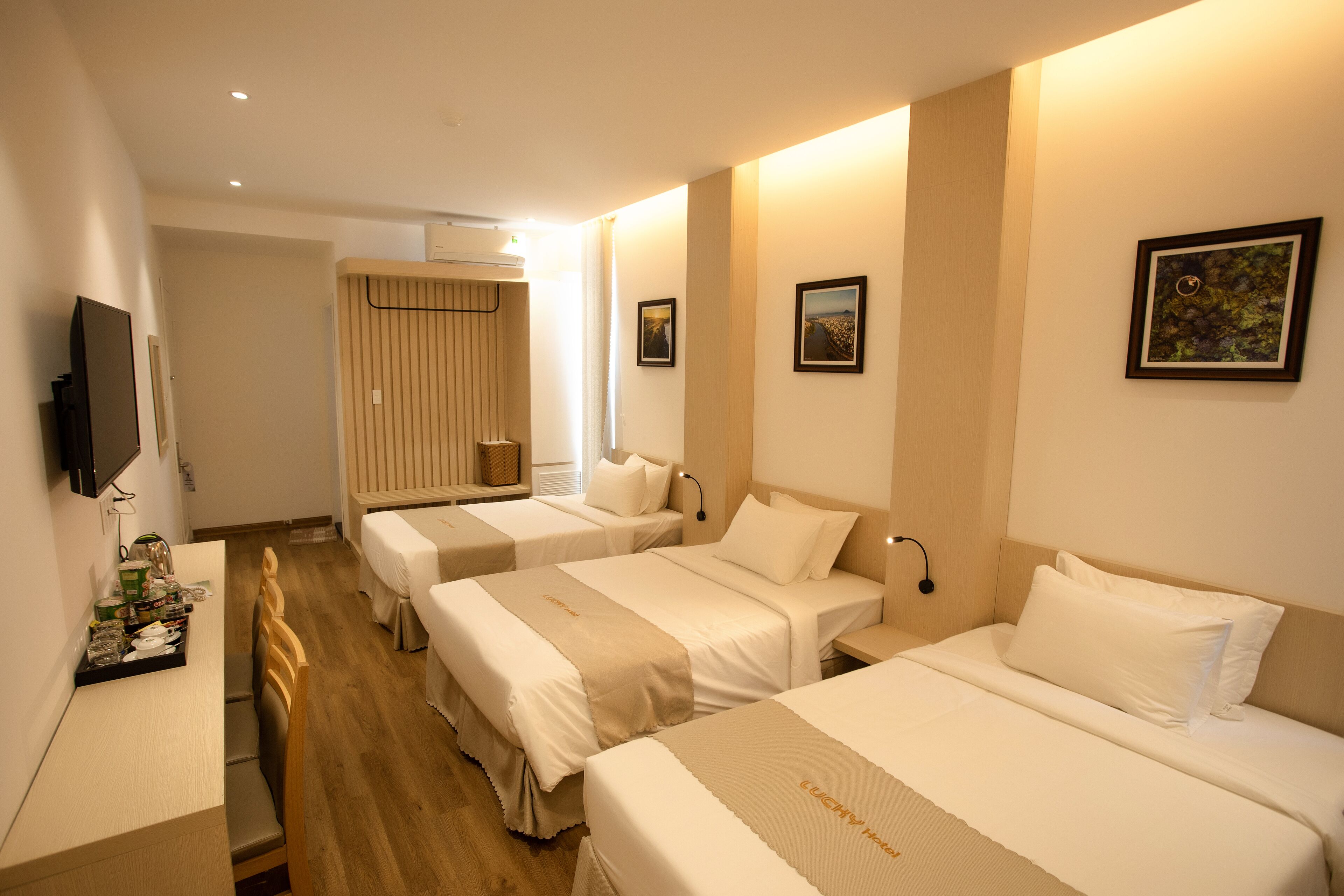 Une chambre d’hôtel avec trois lits simples, un bureau avec une chaise, un téléviseur à écran plat et une fenêtre avec des rideaux.
