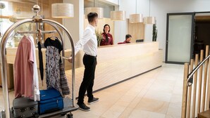 A hotel reception area with a modern design, including a reception desk, a luggage cart, and a mirror reflecting the interior. - Family room Stammhaus category II - Höchsten Natur Erlebnis Hotel (Illmensee)