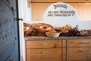 A kitchen counter with various breads and pastries, a sign indicating a daily breakfast service, and wooden cabinets.