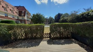 Een houten terras met een bankje, omringd door keurig gesnoeide heggen en een heldere lucht.