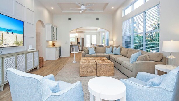 A spacious living room with a large sectional sofa, a TV mounted on the wall, and a dining area in the background.