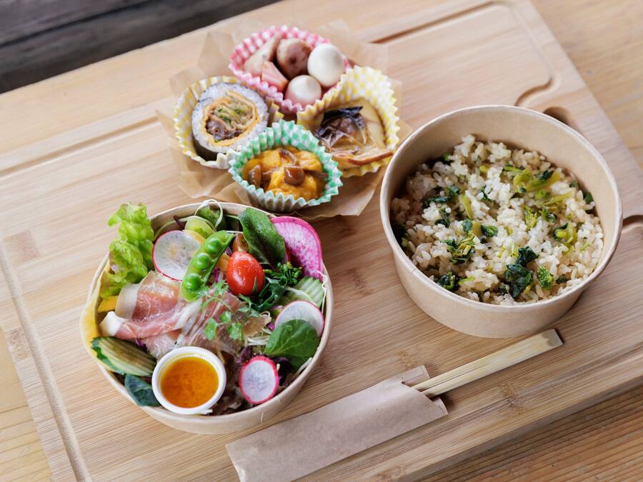 A wooden table with three bowls of food: a salad, rice with greens, and a dish with eggs and meat.