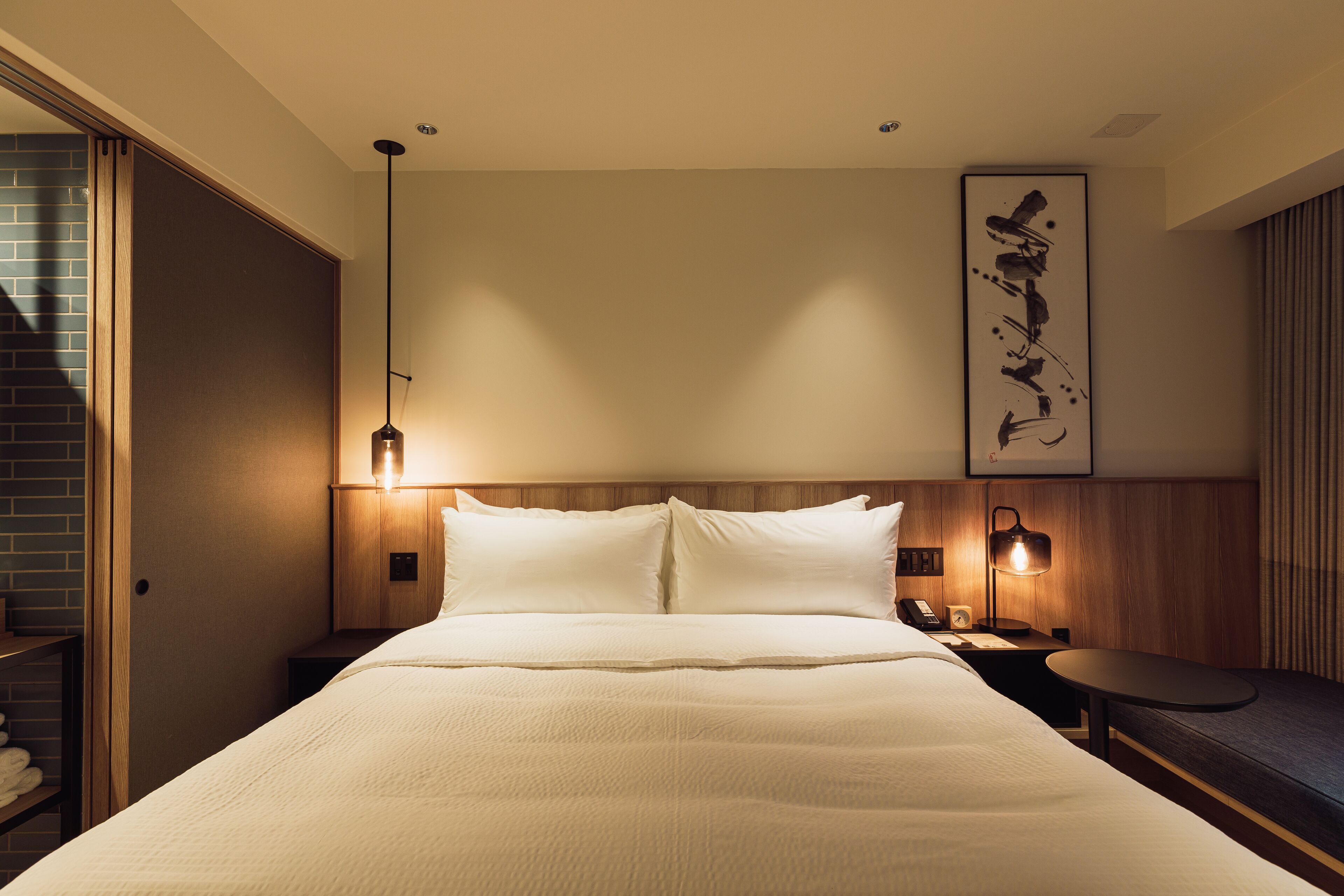 Habitación de hotel con una cama grande, lámparas de noche, un cabecero de madera, una obra de arte en la pared y una mesita.
