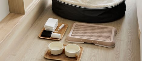 A pet bed, a grooming station, and two bowls on a wooden floor.