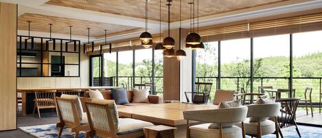Un vaste espace de vie doté d’une grande table en bois, de plusieurs chaises et de luminaires suspendus.