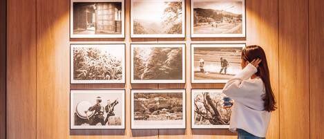 A woman standing in a room with wooden panel walls, looking at framed photographs.