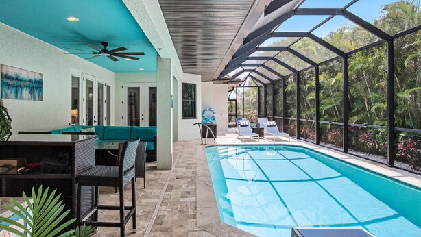 A pool area with a glass-enclosed structure, a ceiling fan, and a seating area with a table and chairs. - Amazing Location - Walk to the Beach & JW ~Fully Loaded Inside & Out w/Pool, Beach Gear, WiFi & More (Marco Island)