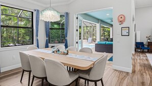 A dining area with a wooden table, four chairs, a chandelier, and a view of an outdoor pool. - Amazing Location - Walk to the Beach & JW ~Fully Loaded Inside & Out w/Pool, Beach Gear, WiFi & More (Marco Island)