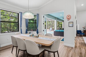 A dining area with a wooden table, four chairs, a chandelier, and a view of an outdoor pool.