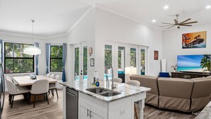 A modern kitchen with a central island, dining area with chairs, a sofa, and a TV. - Amazing Location - Walk to the Beach & JW ~Fully Loaded Inside & Out w/Pool, Beach Gear, WiFi & More (Marco Island)
