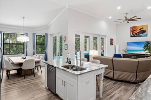 A modern kitchen with a central island, dining area with chairs, a sofa, and a TV.