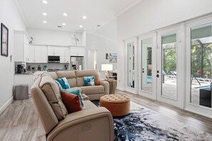 A spacious living room with a beige sofa, ottoman, and a view of a pool through glass doors.
