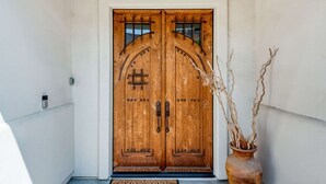 A wooden double door with a metal latch, a doormat, and a potted plant beside it. - Gorgeous Home w/Saltwater Pool/Spa with MISTERS! PGA West - Fabulous Outdoor Setting-3BD#245594 (La Quinta)