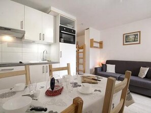A compact living space with a kitchenette, a dining area with a table set for two, and a sofa in the living area.