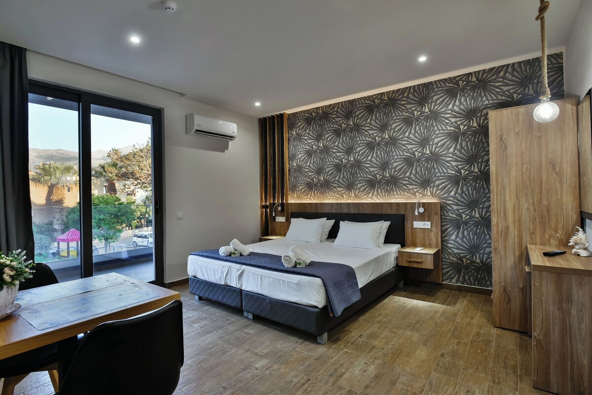 A modern hotel room with a large bed, a dining table, and a view of the outdoors.
