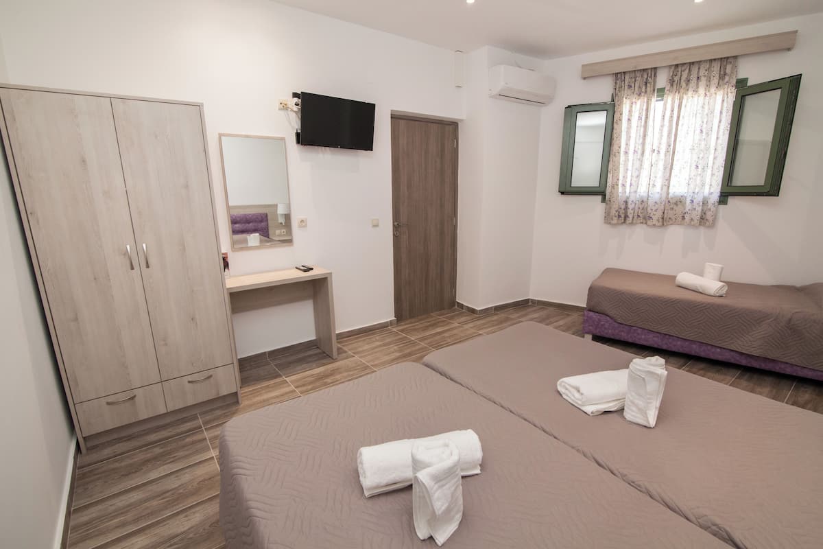 A bedroom with two beds, a wardrobe, a desk, a TV, and a window with curtains.