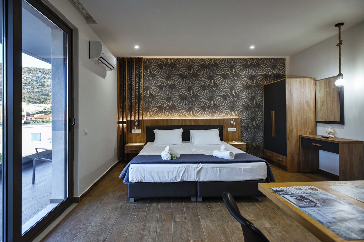 Une chambre d’hôtel moderne dotée d’un grand lit, d’un bureau en bois et donnant sur un espace extérieur grâce à une porte coulissante.