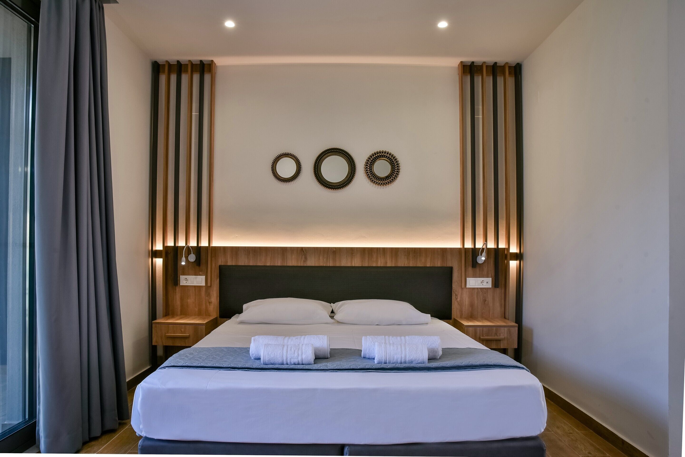 Quarto de hotel moderno com uma cama grande, cabeceira de madeira e duas mesas de cabeceira com abajures.