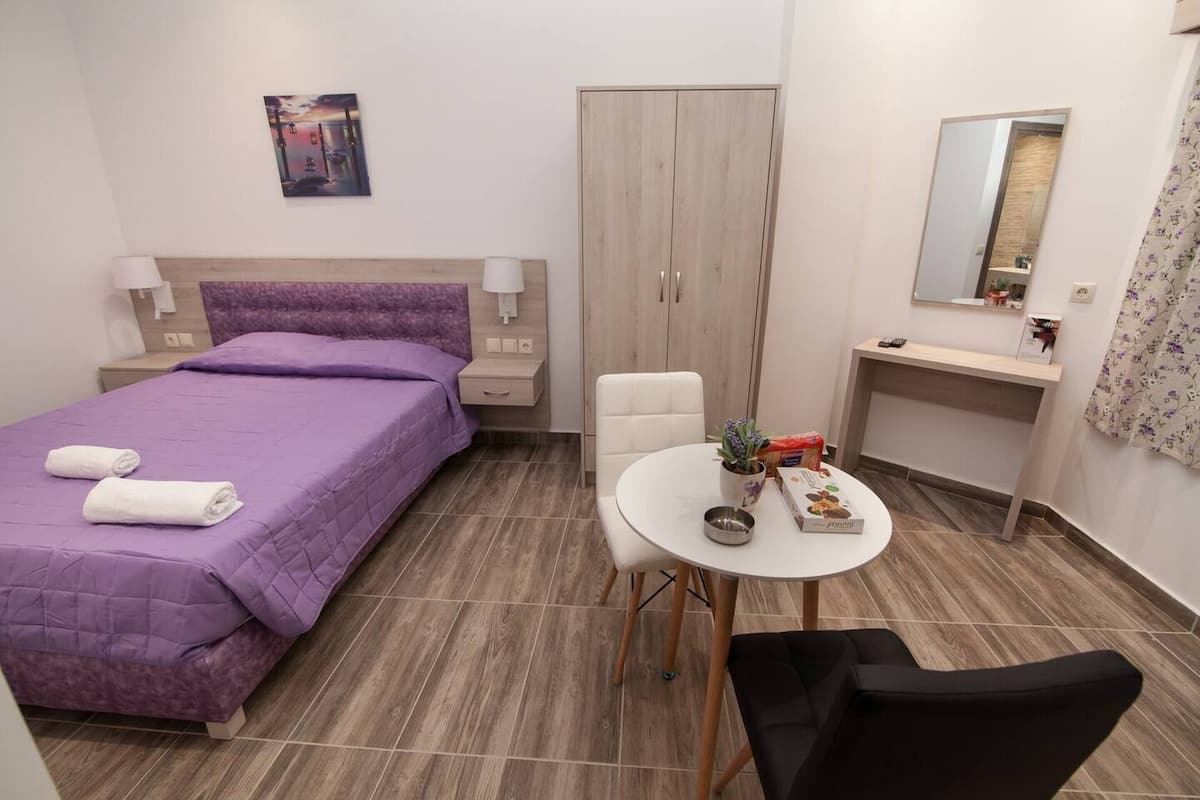 A hotel room with a bed, bedside table, lamp, wardrobe, small round table with a plant, and a mirror.