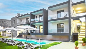 A modern multi-story building with a swimming pool, outdoor seating, and potted plants. - Del Mar Apartments in Stalis (Hersonissos)