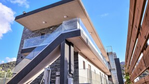 A modern building with a glass balcony, a stone facade, and a clear blue sky in the background. - Del Mar Apartments in Stalis (Hersonissos)
