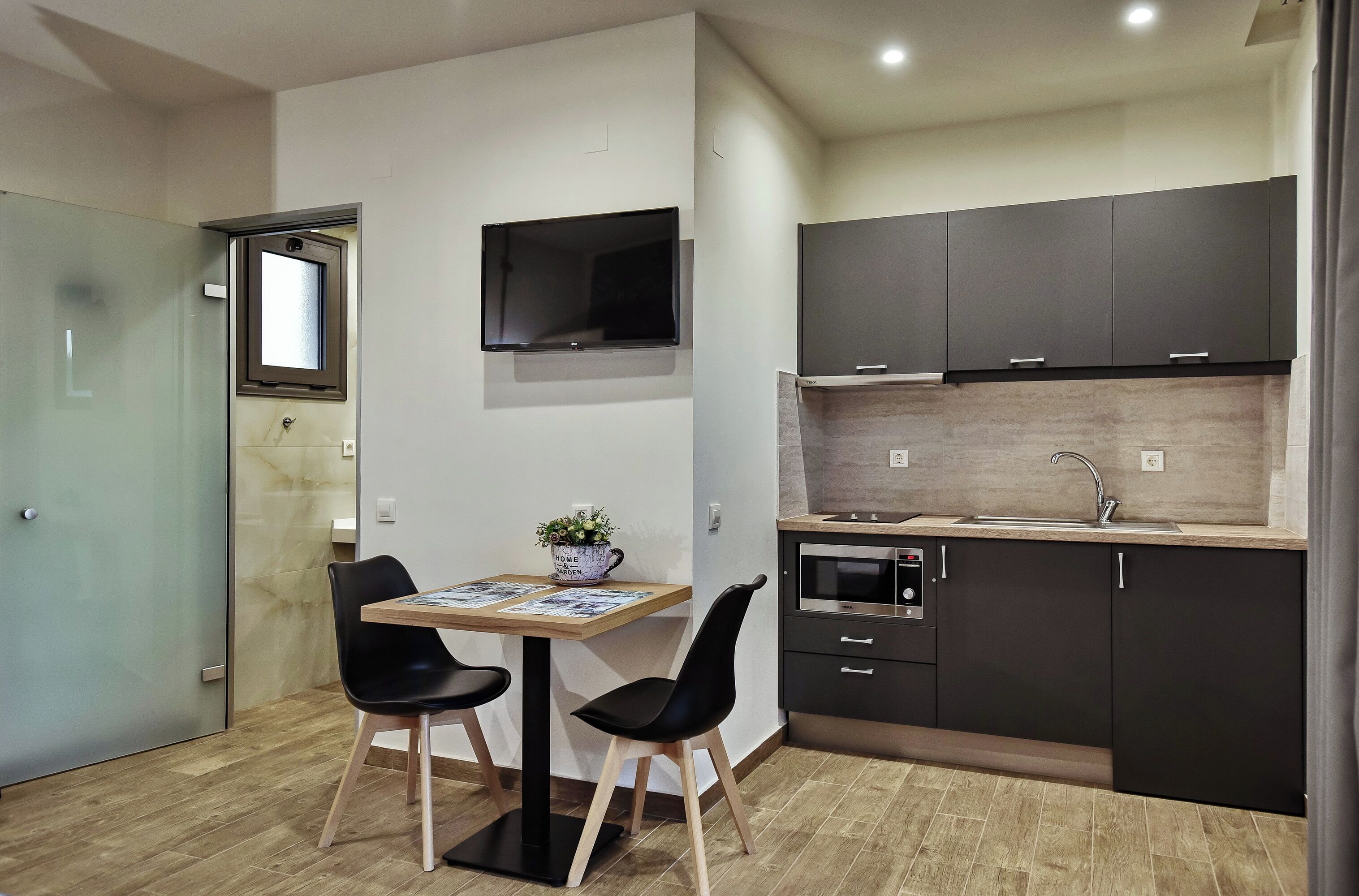 A compact kitchen with dark cabinets, a built-in oven, and a small dining area with two chairs and a table.
