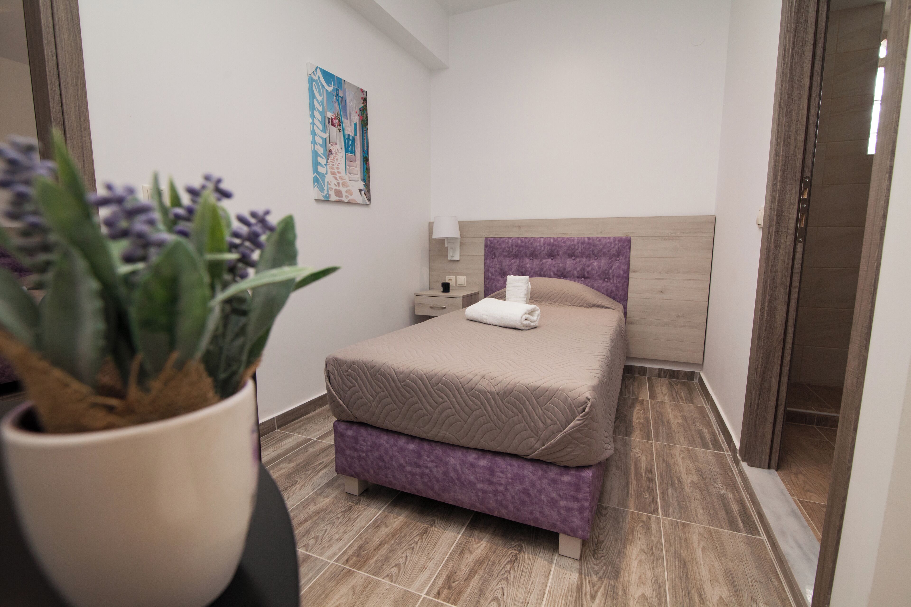 A modern bedroom with a bed, a nightstand, a lamp, and a potted plant.